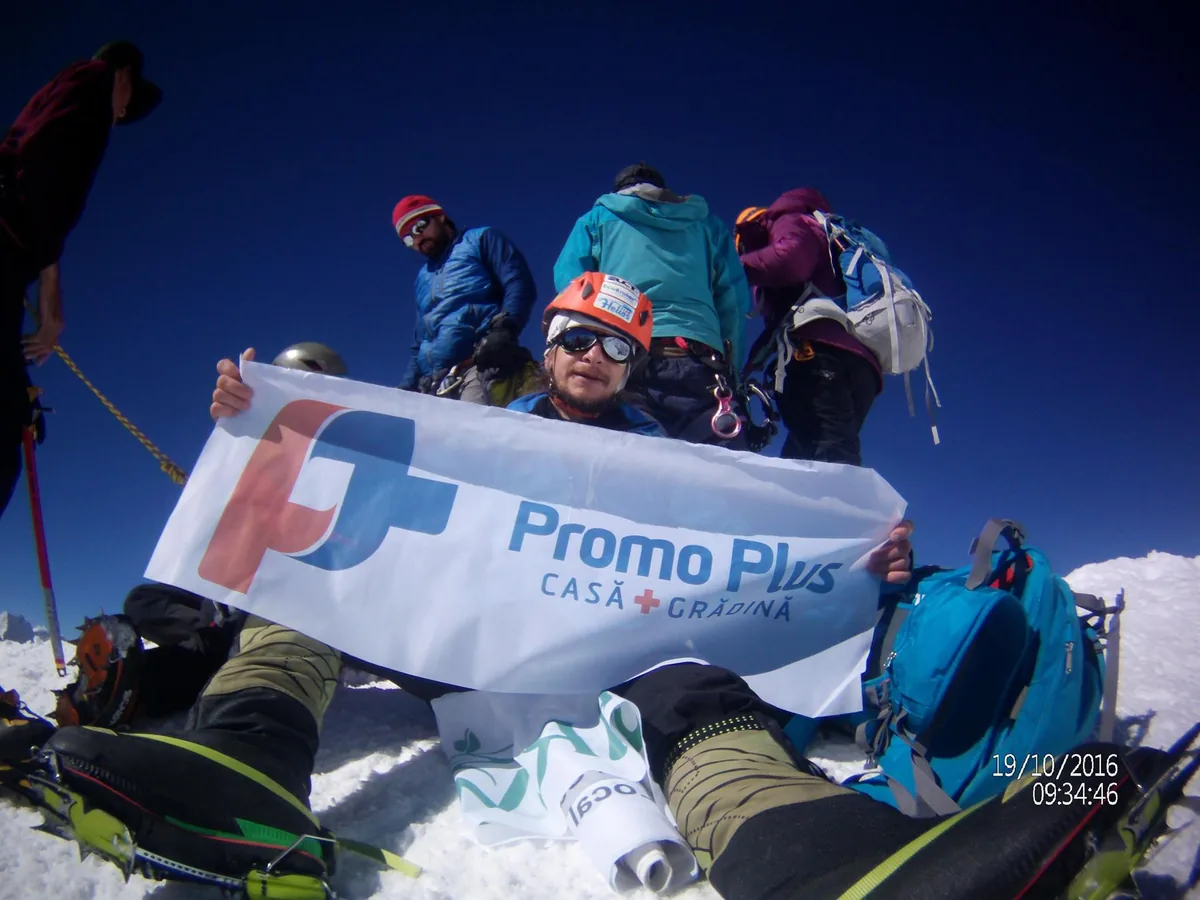 Three climbers holding a Promo Plus flag on a mountain summit